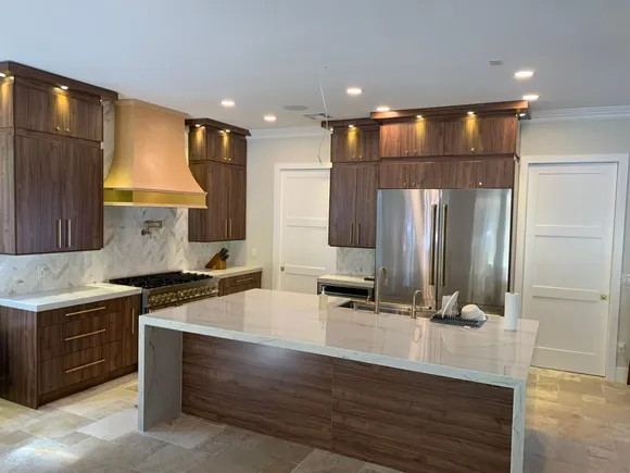 Luxury kitchen featuring a large quartz countertop, dark wood cabinetry, stainless steel appliances, and a sleek range hood.
