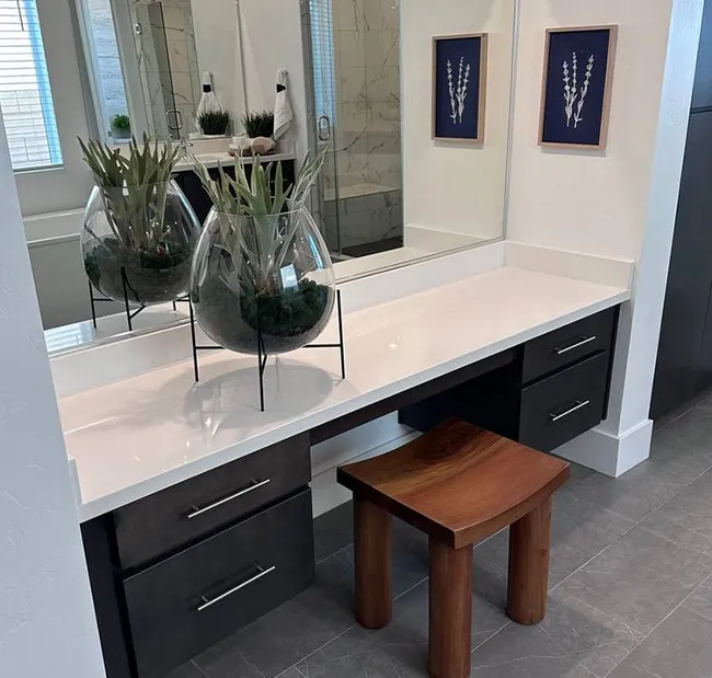 Modern bathroom vanity with white stone countertop, decorative glass planters, and dark cabinetry.